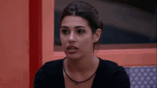 a woman wearing a black sweater and a black necklace is sitting in front of a window and looking at the camera .