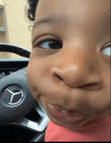 a baby is making a funny face in front of a mercedes steering wheel