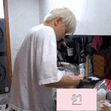 a man in a white shirt is washing dishes in a kitchen with a pink sm entertainment logo in the corner