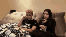 a man and a woman are sitting on a couch with the man wearing a black shirt that says ahava