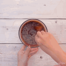 a person is mixing a brown liquid in a glass bowl with a spoon