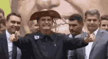 a man wearing a cowboy hat is giving a peace sign while standing in front of a group of men .
