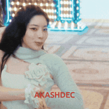 a woman in a white dress with a flower on her chest is standing in front of a sign that says " akashdec "
