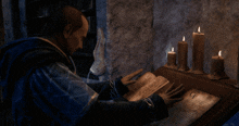 a man sits at a table reading a book with candles in the background