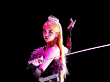 a woman with long blonde hair is wearing a tiara and gloves and holding a sword .