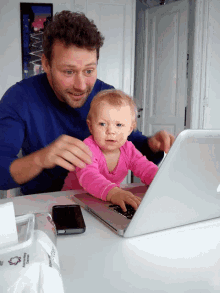 a man holds a baby while using a laptop