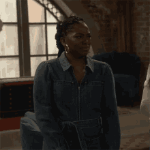 a woman wearing a denim jacket and hoop earrings is standing in front of a window