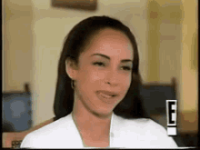 a woman in a white shirt is smiling in front of a sign that says e on it