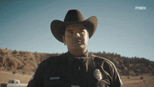 a police officer wearing a cowboy hat is standing in a field
