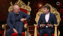 two men are sitting on thrones and one is holding a tablet with the number 10 on the bottom