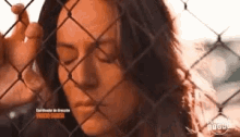 a woman is looking through a chain link fence .