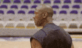 a man in a black tank top is standing on a basketball court in front of empty seats .