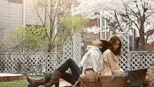 a man and a woman are sitting back to back on a bench under a tree .
