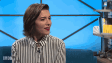 a woman in a striped shirt is sitting in front of a blue screen that says imdb on it