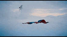 a man in a superman suit is laying in the snow with his mouth wide open