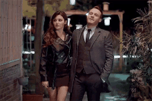 a man and a woman are standing next to each other on a sidewalk at night .