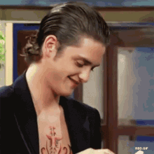 a man with a tattoo on his chest is smiling while wearing a suit jacket