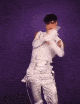 a man in a white tank top and white pants is dancing in front of a purple background .