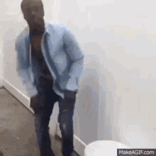 a man in a blue shirt is standing next to a toilet in a bathroom .