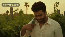 a man in a white shirt is standing in a field with a green cloth around his neck .