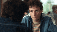 a man with curly hair is looking at another man in a blue jacket