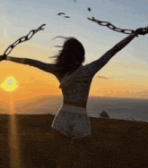 a woman with her arms outstretched holding chains at sunset