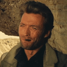 a man with a beard is smoking a cigar in front of a rock wall
