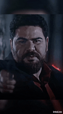 a man with a beard is pointing a gun at the camera with intolive written on the bottom right