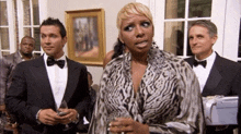a woman in a leopard print dress stands in front of a group of men in tuxedos