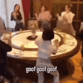 a group of people dancing around a round table with the words goof goof goof written on the bottom
