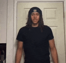 a young man wearing a black shirt and a black beanie stands in front of a door