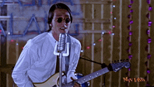 a man is singing into a microphone while holding a guitar in front of a wall that says man laksa