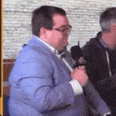 a man in a blue jacket is holding a microphone in front of a brick wall