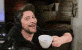 a man wearing headphones holds a white cup of coffee