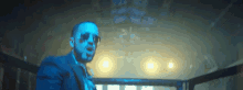 a man in a blue suit and sunglasses stands in a dark room