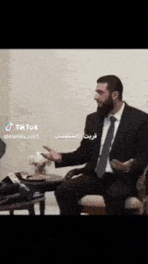 a man in a suit and tie is sitting in front of a table with tiktok written on the bottom right