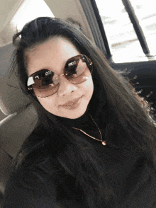 a woman wearing sunglasses and a black turtleneck looks at the camera