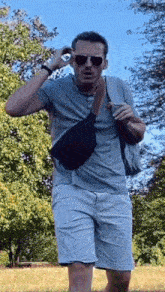 a man wearing sunglasses and a fanny pack is walking through a field