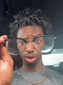 a man wearing glasses and a gold chain looks surprised