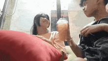 a boy and a girl are sitting on a red pillow and the girl is holding a cup of orange juice