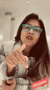 a woman wearing glasses and a plaid shirt is pointing at the camera with a red tag that says oh that solanna