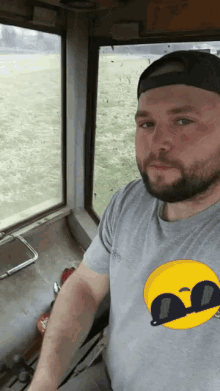 a man with a beard wearing a gray shirt with a yellow smiley face on it
