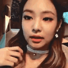 a woman wearing a choker and earrings is looking at the camera .