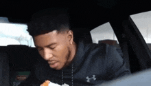 a man in a black under armour shirt is eating a sandwich in a car .