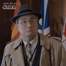 a man wearing glasses and a hat is standing in front of flags with the words son of a grifch written above him