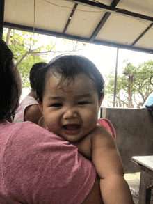 a woman in a pink shirt is holding a baby who is smiling