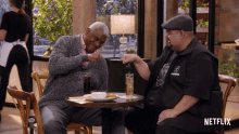 two men sit at a table with a netflix logo on the bottom right