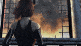 a woman is standing on a balcony looking out a window at an explosion .