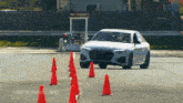 a white car is driving through a row of orange cones on a road