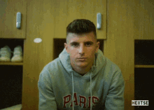 a man wearing a hoodie that says paris is sitting in a locker room